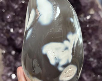 May include: A smooth, white and gray agate stone with a unique, swirling pattern. The stone is polished and has a glossy finish.