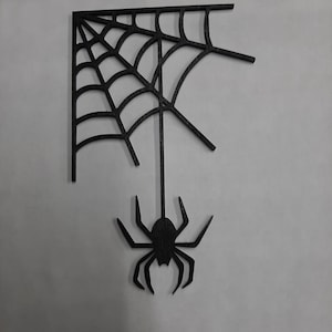 May include: Black wooden cutout of a spider web with a spider hanging from it.