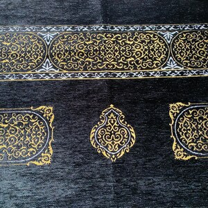 May include: Black prayer rug with gold and white ornate designs. The rug features a central medallion and decorative borders with intricate patterns. The edges are finished with a cream-colored fringe.