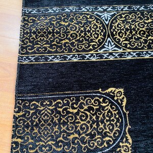 May include: Black prayer rug with gold and white ornate designs. The rug features a central rectangular design with a curved top and bottom, and a border with intricate patterns. The rug is made of a soft, plush material.