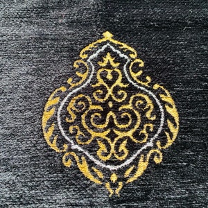 May include: Black prayer rug with an ornate gold and white design. The central motif is a stylized, symmetrical shape with swirling patterns. The rug has a textured surface and a decorative border.