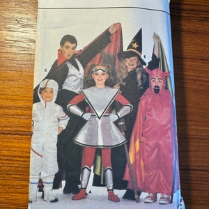 May include: A Butterick pattern envelope featuring a group of children in Halloween costumes. The costumes include a vampire, witch, devil, astronaut, and a futuristic superhero. The envelope is white with the Butterick logo at the top.