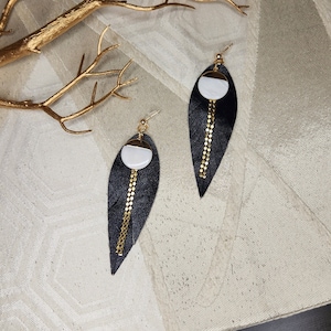May include: A pair of black leather earrings with gold chain accents and a white and gold circle pendant.