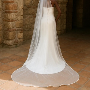 Backside image of a dark-skinned bridal model while wearing a Ivory tulle satin edge veil. The soft beige background highlights her radiant expression and the elegant detailing of the veil.