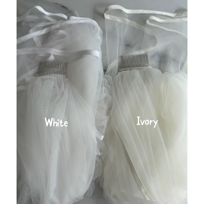 May include: Two bridal veils, one white and one ivory, are displayed. Each veil is attached to a comb and features a soft, flowing fabric. The text "White" and "Ivory" are printed on the veils.