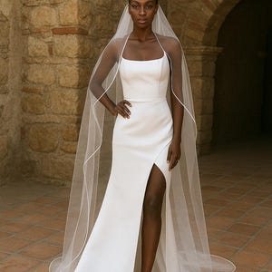 Full Standing Front image of a dark-skinned bridal model while wearing a Ivory tulle satin edge veil. The soft beige background highlights her radiant expression and the elegant detailing of the veil.