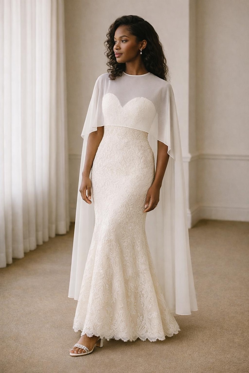 Beautiful bride in a modern white chiffon evening cape dress with a flowing sheer overlay and elegant satin base, standing gracefully against a soft beige background with warm studio lights highlighting her natural beauty. The chiffon cape adds ethereal movement, perfect for bridal photoshoots, rehearsal dinners, or wedding receptions. A minimalist yet luxurious fashion choice for the modern bride seeking timeless elegance.