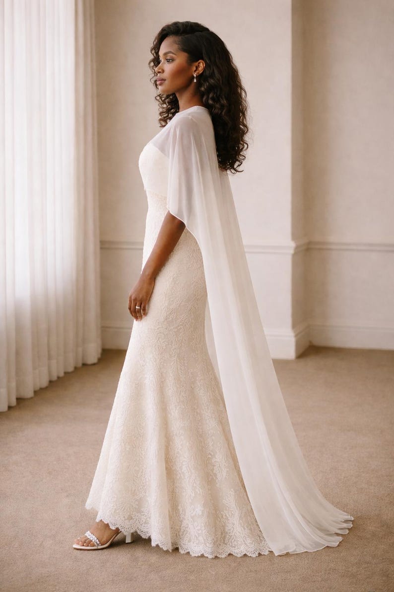 Beautiful bride in a modern white chiffon evening cape dress with a flowing sheer overlay and elegant satin base, standing gracefully against a soft beige background with warm studio lights highlighting her natural beauty. The chiffon cape adds ethereal movement, perfect for bridal photoshoots, rehearsal dinners, or wedding receptions. A minimalist yet luxurious fashion choice for the modern bride seeking timeless elegance.