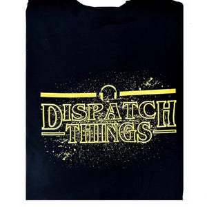 May include: Black t-shirt with a yellow graphic print of the text "DISPATCH THINGS" with a headphone symbol above the text.
