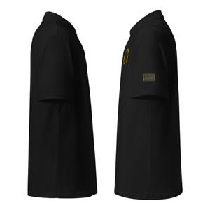 May include: Black polo shirt with a gold embroidered design on the left chest and a small American flag on the right sleeve.