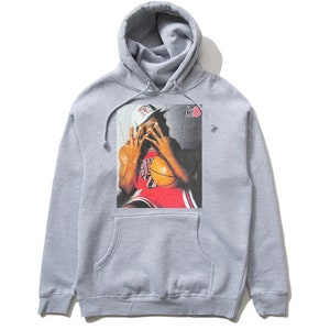 May include: Gray hooded sweatshirt with a graphic print of a basketball player wearing a red jersey and a white hat. The text "k8" is printed on the right side of the graphic.