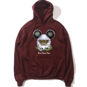 Op de afbeelding: Bordeauxkleurige hoodie met een witte voetbalhelm met Mickey Mouse-oren en de tekst "Your Name Here" op de voorkant.