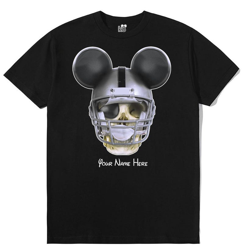 Puede incluir: Camiseta negra con un gr&aacute;fico de una calavera con un casco de f&uacute;tbol americano y orejas de Mickey Mouse. El texto "Your Name Here" est&aacute; impreso debajo del gr&aacute;fico.