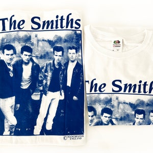 May include: White t-shirt with a blue print of the band The Smiths. The print features a photo of the band members and the band's name in bold blue letters.
