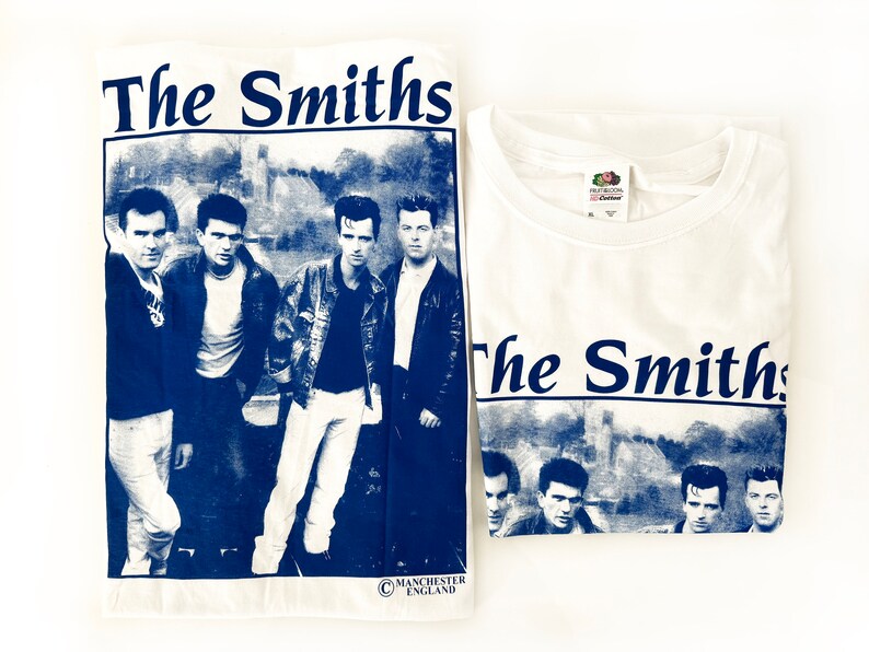May include: White t-shirt with a blue print of the band The Smiths. The print features a photo of the band members and the band's name in bold blue letters.