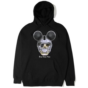 Puede incluir: Sudadera con capucha negra con una calavera con un casco de f&uacute;tbol americano y orejas de Mickey Mouse. El texto "Your Name Here" est&aacute; impreso debajo de la calavera.