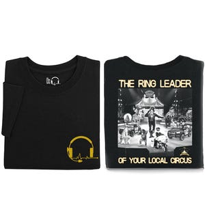 May include: A black short-sleeve t-shirt featuring a yellow headset graphic on the front. The back displays a black and white circus scene with the text THE RING LEADER OF YOUR LOCAL CIRCUS in yellow, along with a small dispatch center logo.