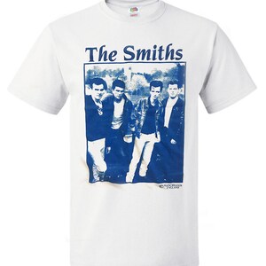 May include: White t-shirt with a blue and white image of the band The Smiths. The image shows four men in a band, with the text "The Smiths" above the image and "Manchester England" below the image.