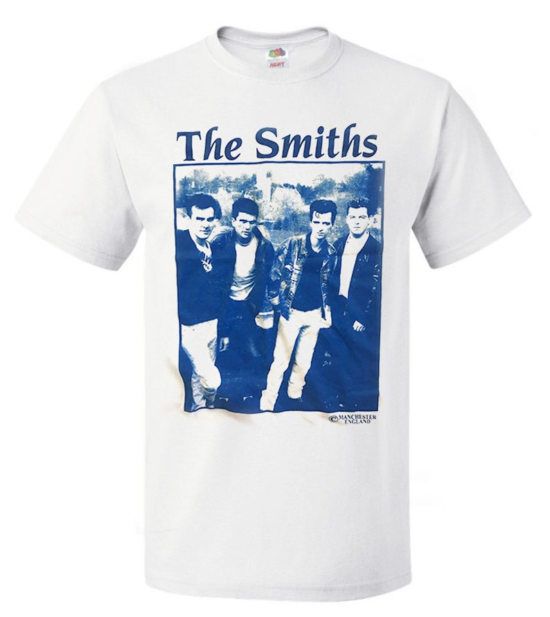 May include: White t-shirt with a blue and white image of the band The Smiths. The image shows four men in a band, with the text "The Smiths" above the image and "Manchester England" below the image.