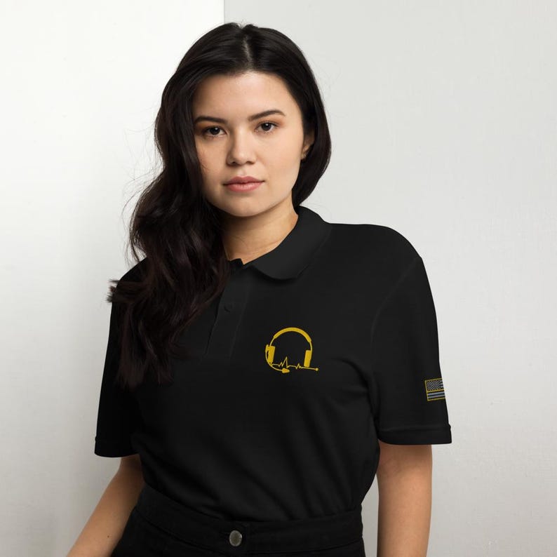 May include: Black polo shirt with a gold outline of headphones and a heartbeat graphic. The shirt has a small American flag on the sleeve.