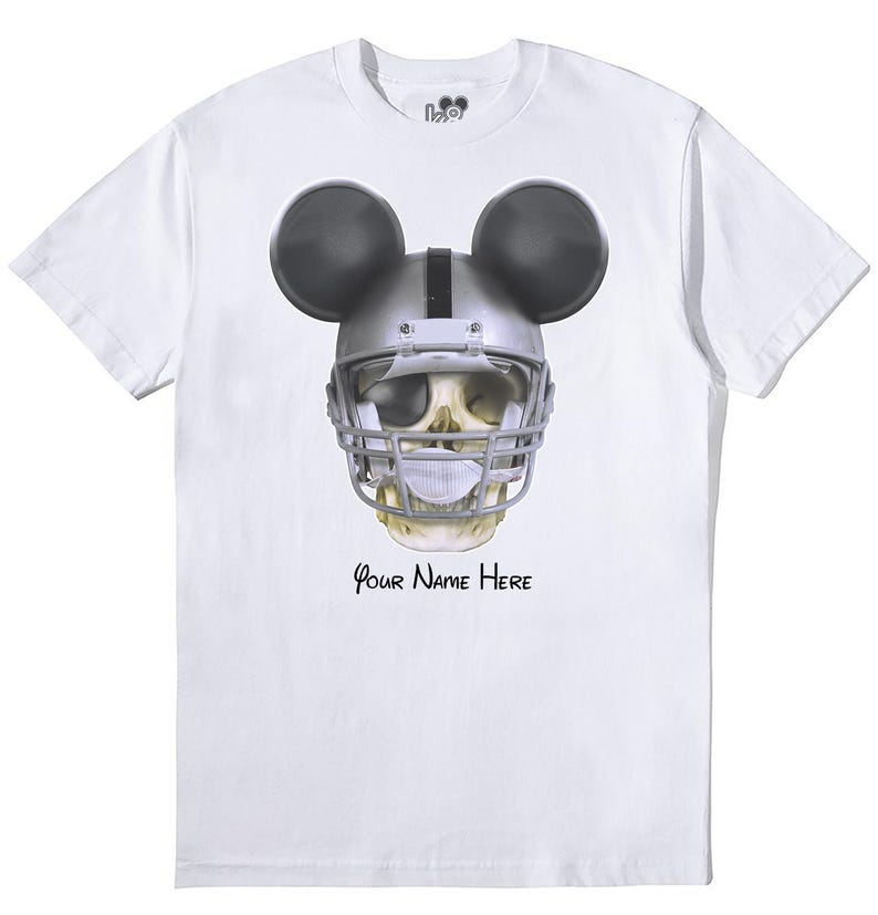 Puede incluir: Camiseta blanca con un gr&aacute;fico de una calavera con un casco de f&uacute;tbol americano y orejas de Mickey Mouse. El texto "Your Name Here" est&aacute; impreso debajo del gr&aacute;fico.