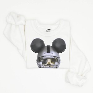 Puede incluir: Camiseta blanca de manga larga con una calavera negra y plateada que lleva un casco de f&uacute;tbol americano y orejas de Mickey Mouse.