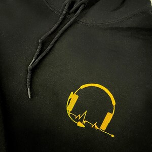 May include: Black hoodie with a gold embroidered design of headphones and a heartbeat line.