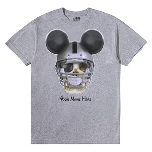 Puede incluir: Camiseta gris con una calavera con un casco de f&uacute;tbol americano y orejas de Mickey Mouse. El texto "Your Name Here" est&aacute; impreso debajo de la calavera.