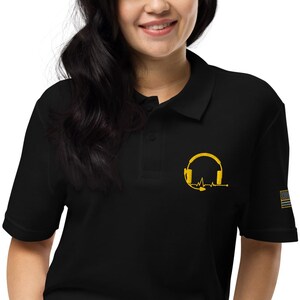 May include: Black polo shirt with a gold embroidered design of a headset with a heartbeat line. The shirt also has a small American flag patch on the sleeve.