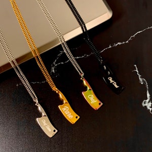 May include: Four silver chains with knife-shaped pendants. The pendants are engraved with the words "Chef Dad", "Chef", "Rare", and "Chef Sam".