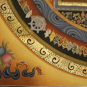 May include: A close-up of a corner of a Tibetan mandala painting. The mandala is painted on a gold background with intricate details in black, blue, and red. The mandala features a wheel of dharma, a symbol of Buddhist teachings.