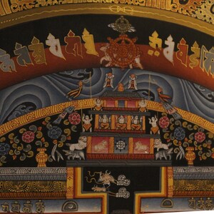 May include: A colorful Tibetan Buddhist mandala painting with intricate details. The painting features a central motif of a wheel with spokes, surrounded by a circular border of stylized clouds and floral patterns. The painting is framed by a gold border with ornate designs.