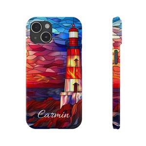 May include: A phone case featuring a stained-glass style lighthouse design. The lighthouse is red, white, and yellow, set against a sunset sky of red, orange, and blue. The name "Carmin" is written on the case.