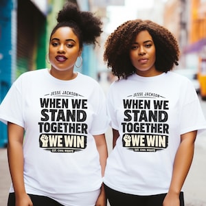 May include: Two people wearing white t-shirts with the text "WHEN WE STAND TOGETHER WE WIN" and "EST. CIVIL RIGHTS" printed in black. The shirts feature the name "JESSE JACKSON" above the text and a fist graphic. The people are standing in front of a blurred urban background.