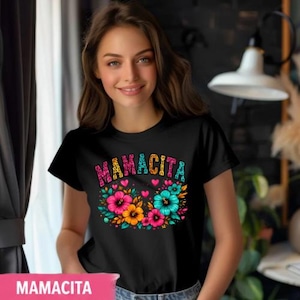 May include: Black t-shirt with the word "MAMACITA" in colorful letters above a floral design. The flowers are pink, orange, and teal. The shirt is short-sleeved.