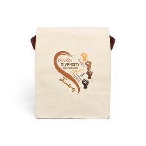 May include: Cream-colored tote bag with brown handles and a heart-shaped graphic. The graphic includes the words "Progress, Diversity, Kindness, Community, Equality, Love, Strength" and a series of raised fists in various skin tones. The name "Kimberly" is also featured.