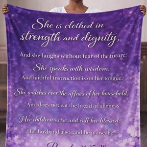 Peut inclure: Une couverture violette avec une citation blanche de Proverbes 31:25-28. La couverture présente un motif floral en bas et est tenue par une personne.