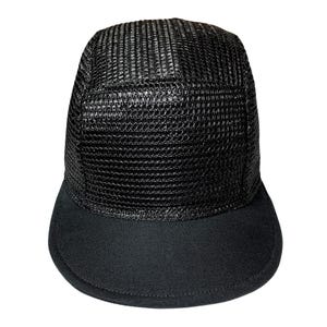 Può includere: Un cappellino da baseball nero con la parte superiore in rete e la visiera solida. Il cappellino ha un design strutturato e una visiera curva. Il materiale a rete sulla parte superiore ha un aspetto strutturato. La visiera è in tessuto liscio.