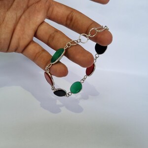 May include: A silver bracelet with oval-shaped green, red, and black stones.