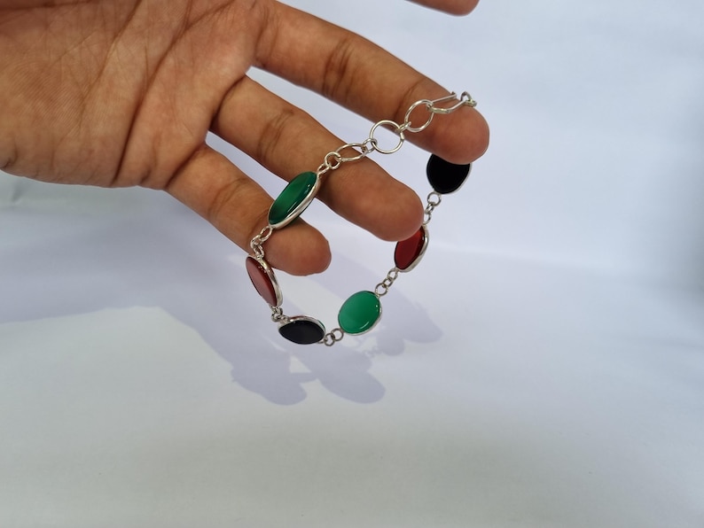 May include: A silver bracelet with oval-shaped green, red, and black stones.