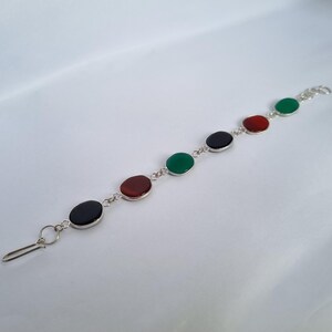 May include: A silver bracelet with five oval-shaped gemstones. The gemstones are green, red, black, red, and green.
