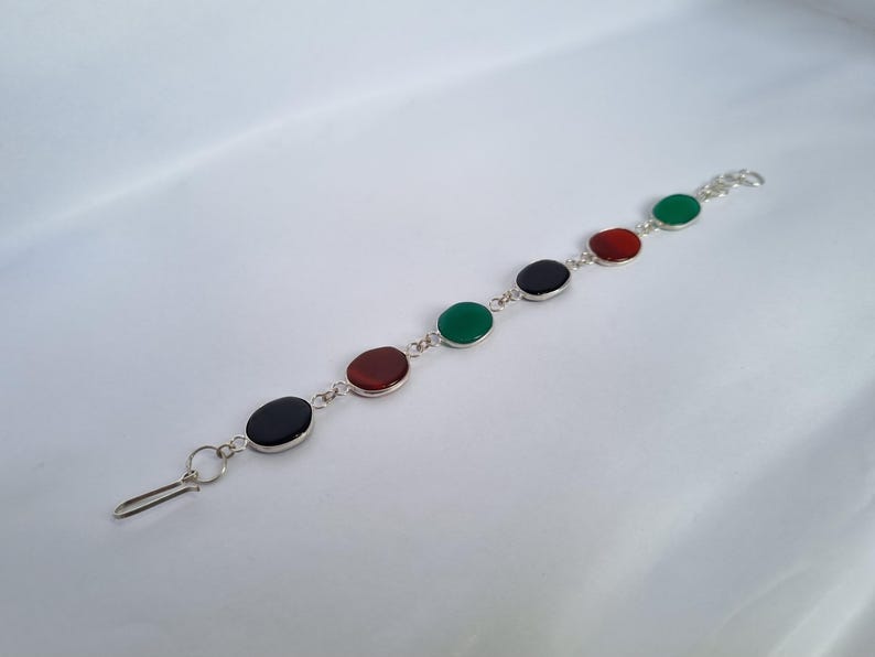 May include: A silver bracelet with five oval-shaped gemstones. The gemstones are green, red, black, red, and green.