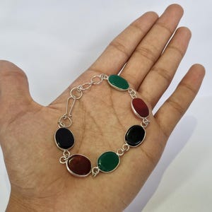 May include: A silver bracelet with oval-shaped gemstones in black, green, and red.