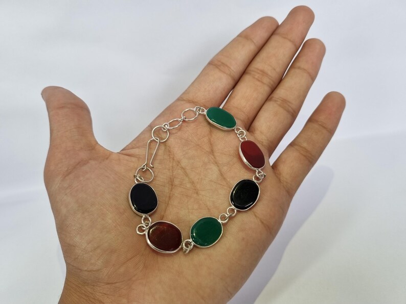 May include: A silver bracelet with oval-shaped gemstones in black, green, and red.