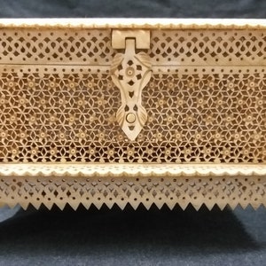 May include: A small, intricately carved wooden box with a hinged lid and a decorative latch. The box is made of light-colored wood and has a delicate, floral pattern carved into its surface.