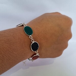 May include: A silver bracelet with green, black, and orange oval-shaped stones.