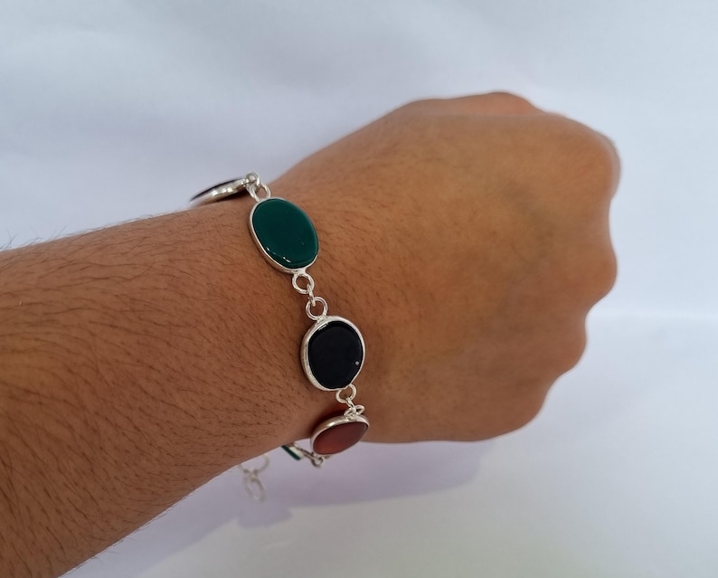 May include: A silver bracelet with green, black, and orange oval-shaped stones.