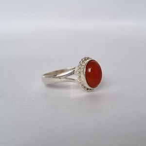 May include: A silver ring with a red carnelian gemstone set in a twisted rope design.