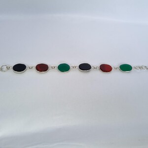 May include: A silver bracelet with oval-shaped gemstones in black, red, and green.