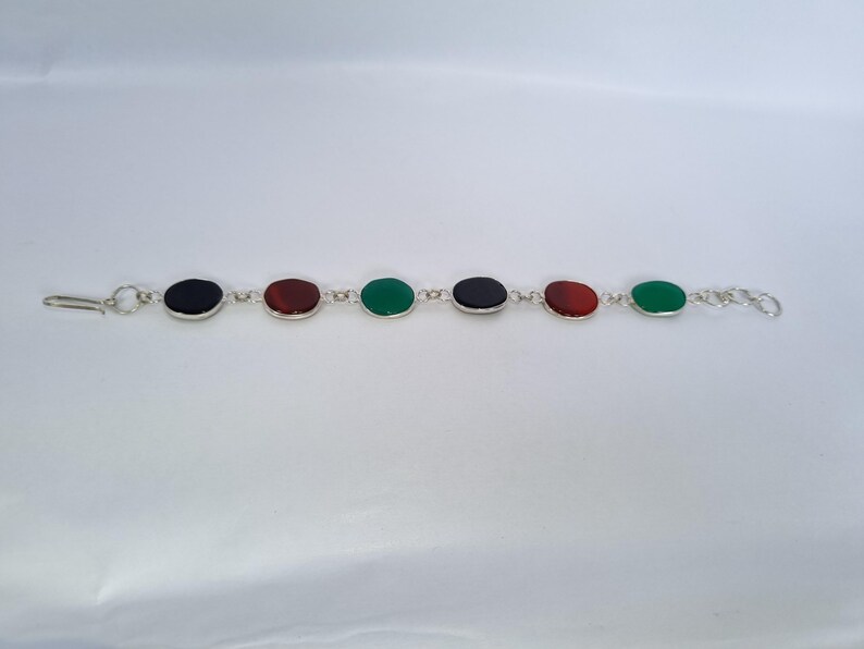 May include: A silver bracelet with oval-shaped gemstones in black, red, and green.